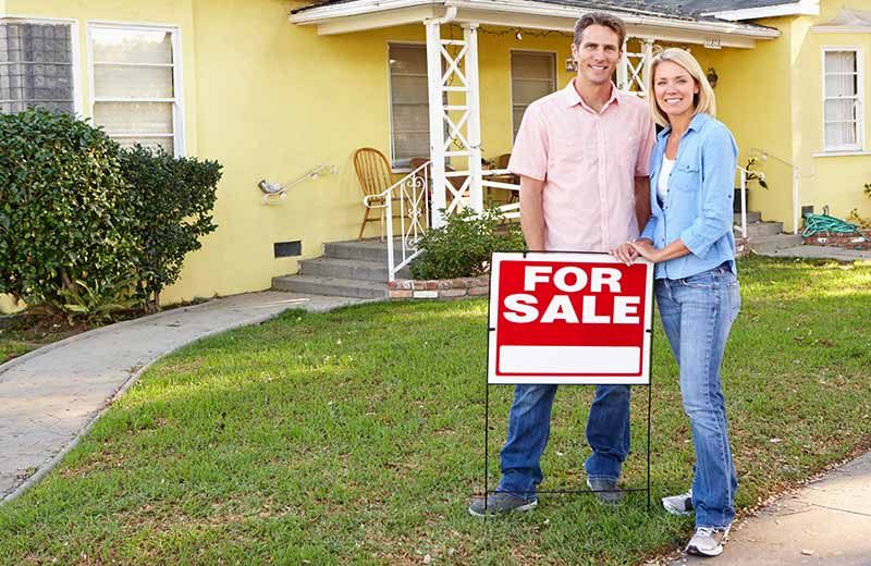 Couple standing in front yard next to For Sale sign waiting for pre-purchase inspections.